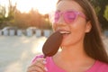 Beautiful young woman eating ice cream glazed in chocolate on city street, closeup Royalty Free Stock Photo