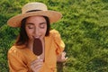Beautiful young woman eating ice cream glazed in chocolate on green grass outdoors. Space for text Royalty Free Stock Photo