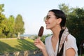 Beautiful young woman eating ice cream glazed in chocolate outdoors, space for text Royalty Free Stock Photo