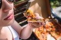 Beautiful, young woman eating pizza in the street. The concept of fast food, food delivery and lunch in nature Royalty Free Stock Photo