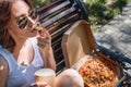 Beautiful, young woman eating pizza in the street. The concept of fast food, food delivery and lunch in nature Royalty Free Stock Photo