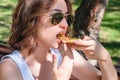 Beautiful, young woman eating pizza in the street. The concept of fast food, food delivery and lunch in nature Royalty Free Stock Photo