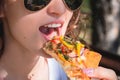 Beautiful, young woman eating pizza in the street. The concept of fast food, food delivery and lunch in nature Royalty Free Stock Photo
