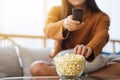 A beautiful young woman eating pop corn and searching channel with remote control to watch tv while sitting on Royalty Free Stock Photo