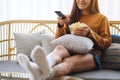 A beautiful young woman eating pop corn and searching channel with remote control to watch tv while sitting on Royalty Free Stock Photo