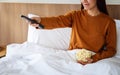 A beautiful young woman eating pop corn and searching channel with remote control to watch tv while sitting in Royalty Free Stock Photo