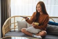 A beautiful young woman eating pop corn and searching channel with remote control to watch tv while sitting on Royalty Free Stock Photo