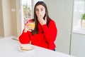 Beautiful young woman eating toasts and orange juice for snack or breakfast cover mouth with hand shocked with shame for mistake,