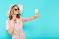 Beautiful young woman in elegant pale pink dress, sunglasses and summer hat taking selfie. Studio portrait of fashionable woman.