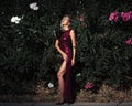 Beautiful young woman in elegant red dress on leaves backdrop. Fashion concept. Hard light