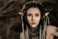 Beautiful young woman with elf ears, dreadlocks and an ethnic poncho, with painted face. Posing against a sandy career Royalty Free Stock Photo