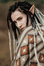 Beautiful young woman with elf ears, dreadlocks and an ethnic poncho, with painted face. Posing against a sandy career Royalty Free Stock Photo