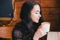 Beautiful young woman enjoying coffee cappuccino with foam near window