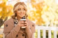 Beautiful young woman enjoying coffee smell in the park in autumn