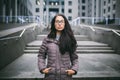 Beautiful young woman of European ethnicity with long brunette hair, wearing glasses and a coat stands against backdrop of a busin Royalty Free Stock Photo