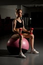 Beautiful young woman exercising with dumbbells on fitness ball at gym against mirror Royalty Free Stock Photo