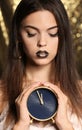 Beautiful young woman with extravagant makeup holding clock against defocused lights Royalty Free Stock Photo