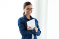 Beautiful young woman with eyeglasses looking at camera while holding digital tablet over white background. Royalty Free Stock Photo