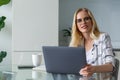 beautiful young woman in eyeglasses using laptop and looking at camera while working