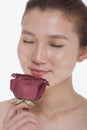 Beautiful young woman with eyes closed smelling a red rose, studio shot Royalty Free Stock Photo