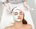 Beautiful young woman with facial mask in beauty salon. Girl getting beauty treatment facial care by beautician Royalty Free Stock Photo
