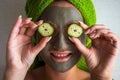 Beautiful young woman with facial mask on her face holding slices of cucumber Royalty Free Stock Photo