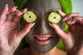 Beautiful young woman with facial mask on her face holding slices of cucumber Royalty Free Stock Photo