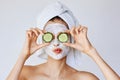 Beautiful young woman with facial mask on her face holding slices of cucumber. Skin care and treatment, spa, natural beauty and Royalty Free Stock Photo