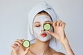 Beautiful young woman with facial mask on her face holding slices of cucumber. Skin care and treatment, spa, natural beauty and Royalty Free Stock Photo