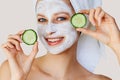 Beautiful young woman with facial mask on her face holding slices of cucumber. Skin care and treatment, spa, natural beauty and Royalty Free Stock Photo