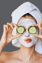 Beautiful young woman with facial mask on her face holding slices of cucumber. Skin care and treatment, spa, natural beauty and Royalty Free Stock Photo