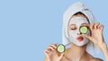 Beautiful young woman with facial mask on her face holding slices of cucumber. Skin care and treatment, spa, natural beauty and Royalty Free Stock Photo