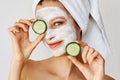 Beautiful young woman with facial mask on her face holding slices of cucumber. Skin care and treatment, spa, natural beauty and