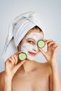 Beautiful young woman with facial mask on her face holding slices of cucumber. Skin care and treatment, spa, natural beauty and Royalty Free Stock Photo