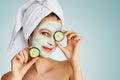 Beautiful young woman with facial mask on her face holding slices of cucumber. Skin care and treatment, spa, natural beauty and Royalty Free Stock Photo