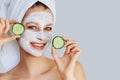 Beautiful young woman with facial mask on her face holding slices of cucumber. Skin care and treatment, spa, natural beauty and Royalty Free Stock Photo