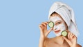 Beautiful young woman with facial mask on her face holding slices of cucumber. Skin care and treatment, spa, natural beauty and Royalty Free Stock Photo