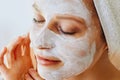 Beautiful young woman with facial mask on her face. Skin care and treatment, spa, natural beauty and cosmetology concept