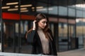 Beautiful young woman fashion model in trendy wear straightens chic hair outdoors on a spring day. Elegant European girl in a Royalty Free Stock Photo