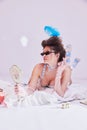Beautiful young woman with feather head accessories and sunglasses lying on bed in vintage lingerie and looking on Royalty Free Stock Photo
