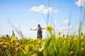 Beautiful young woman on a field with green grass and yellow dandelion flowers in a sunny day. Girl with small dog on nature Royalty Free Stock Photo