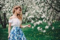 Beautiful young woman in floral maxi skirt walking in blooming spring garden