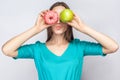 Beautiful young woman with freckles in green dress, holding before her eyes green apple and pink donut and kissing. Royalty Free Stock Photo