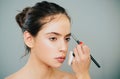 Beautiful young woman getting eyebrow make-up. The artist is applying eyeshadow on her eyebrow with brush. Young model Royalty Free Stock Photo