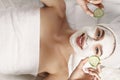 Beautiful young woman is getting facial clay mask at spa, lying with cucumbers on eyes. skin care. Royalty Free Stock Photo