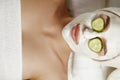 Beautiful young woman is getting facial clay mask at spa, lying with cucumbers on eyes. Royalty Free Stock Photo