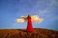 Beautiful young woman or girl in red dress and white wings on the sand on sunny day with blue sky. Angel model or dancer Royalty Free Stock Photo