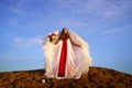 Beautiful young woman or girl in red dress and white wings on the sand on sunny day with blue sky. Angel model or dancer Royalty Free Stock Photo