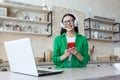 Beautiful young woman in glasses and green shirt relaxing at home in kitchen, listening music Royalty Free Stock Photo