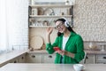 Beautiful young woman in glasses and green shirt relaxing at home in kitchen, listening music Royalty Free Stock Photo